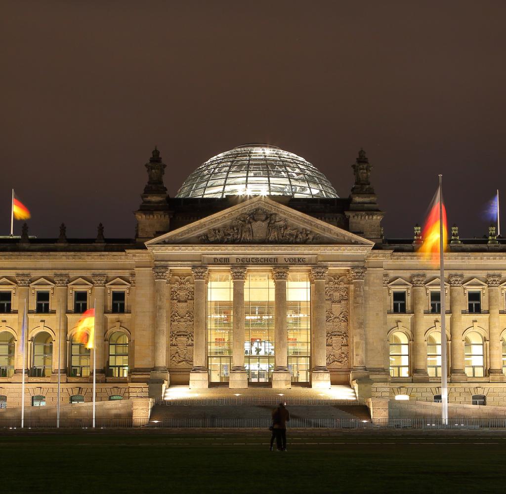 Long exposure of German flags on Bundestag in Berlin at night, silhouette of couple