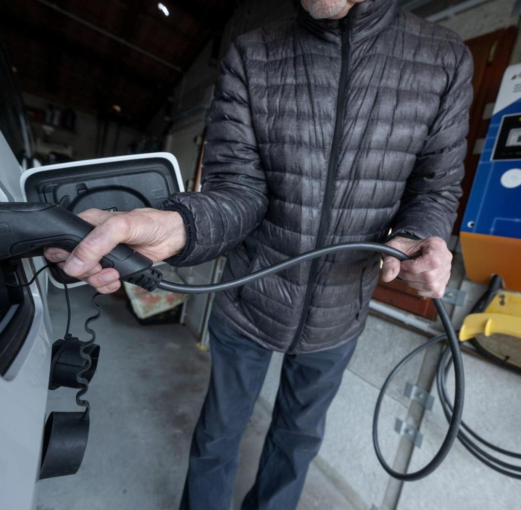 Der Fahrer eines Elektroautos stöpselt zuhause den Ladestecker ein
